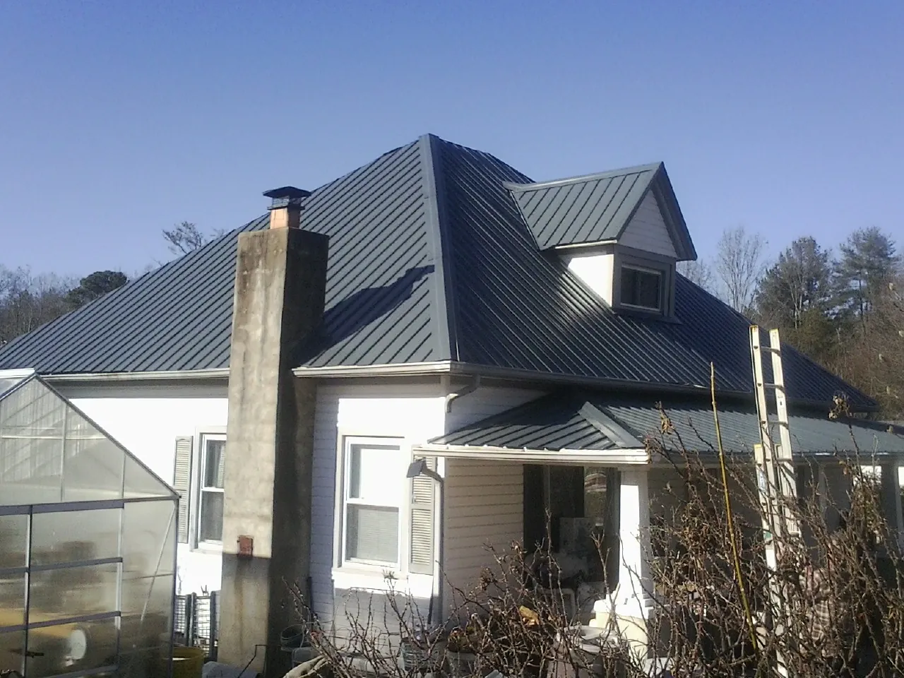 Dark blue standing seam metal roof on a white farmhouse with dormer — Slate & Tile Roof Repair by Roofing Brothers in Oreland