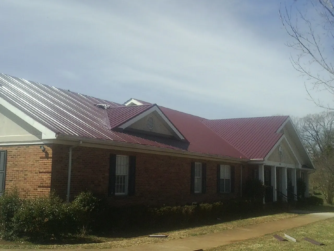 Red metal roof with gabled entries on a long brick building, from a Hail Damage Roof Repair job in Oreland