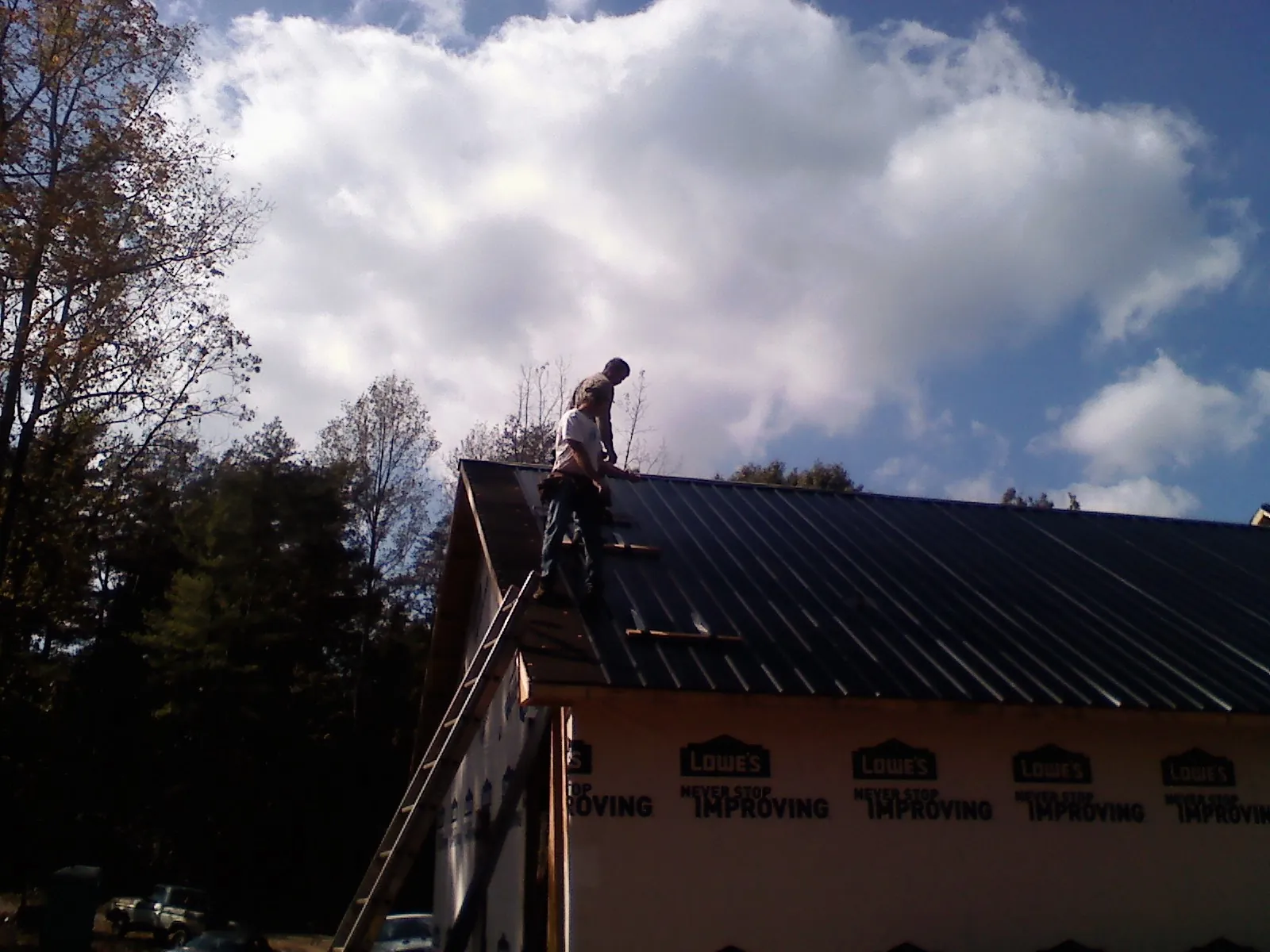 Roofer fastening dark metal panels high against a cloudy sky, from a Roof Inspection job in Oreland