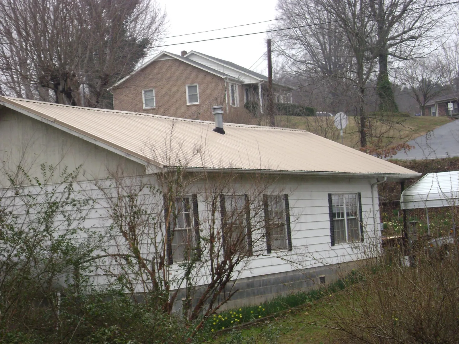 Tan metal roof on a white sided house set into a hillside — Commercial Roofing by Roofing Brothers in Oreland